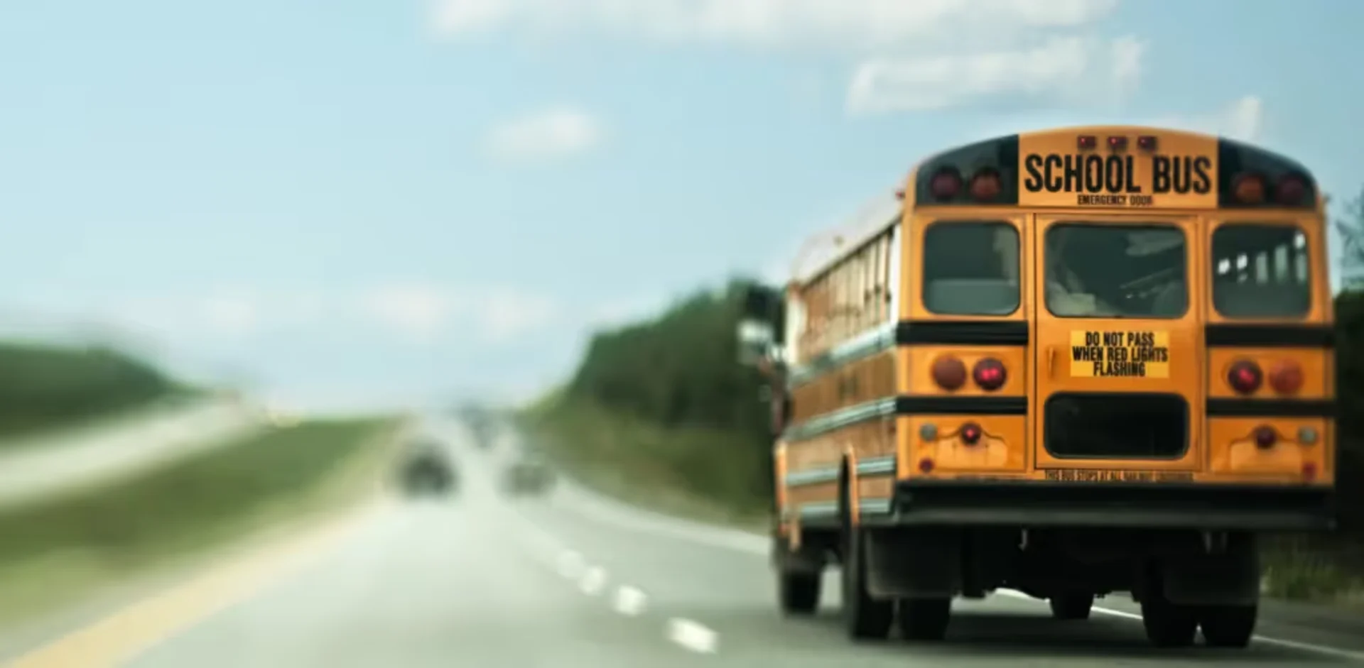 Rear view of a yellow school bus traveling on a highway with DO NOT PASS WHEN RED LIGHTS FLASHING warning sign visible