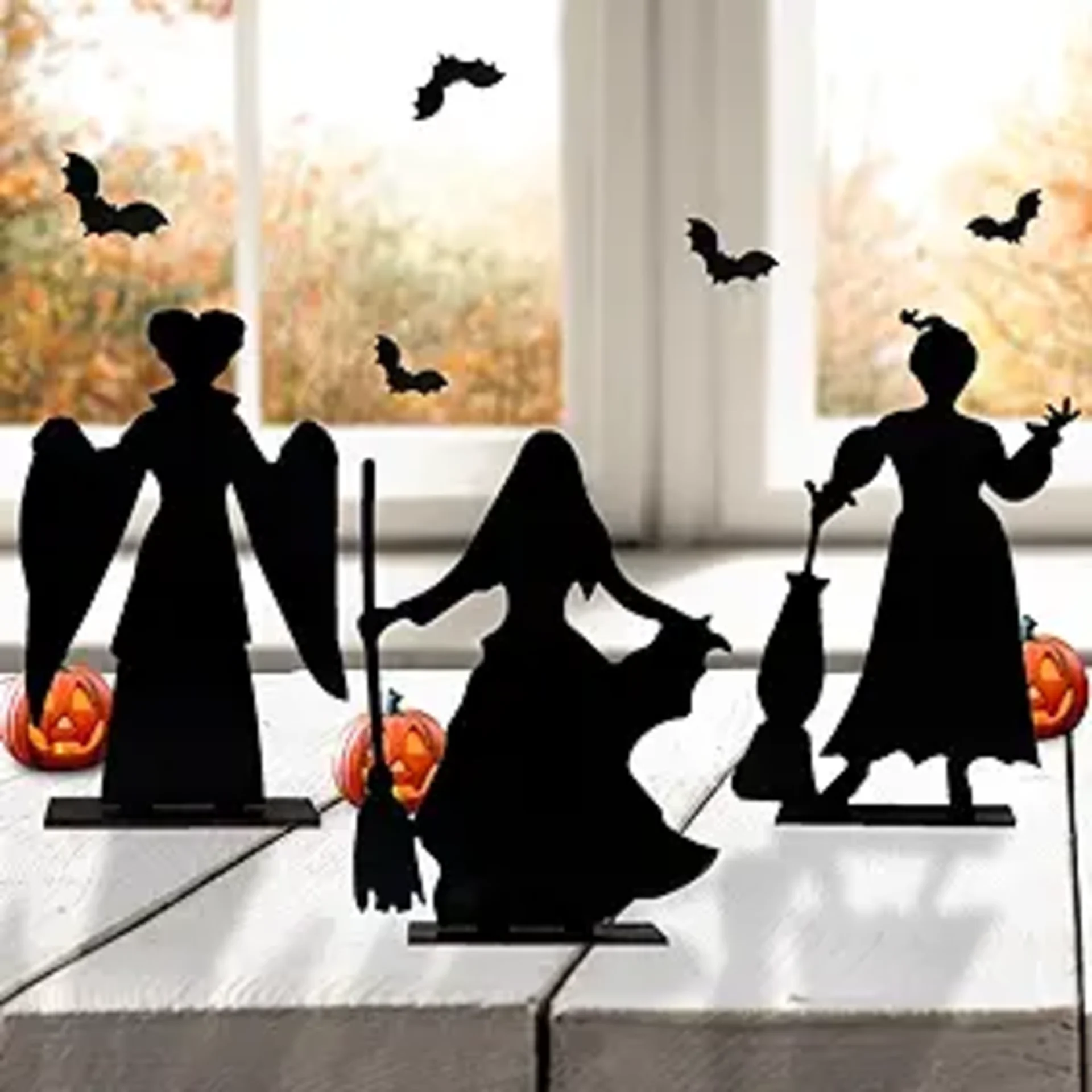 Three black silhouette witch figurines inspired by Hocus Pocus displayed on a white table with glowing jack-o-lanterns and ba