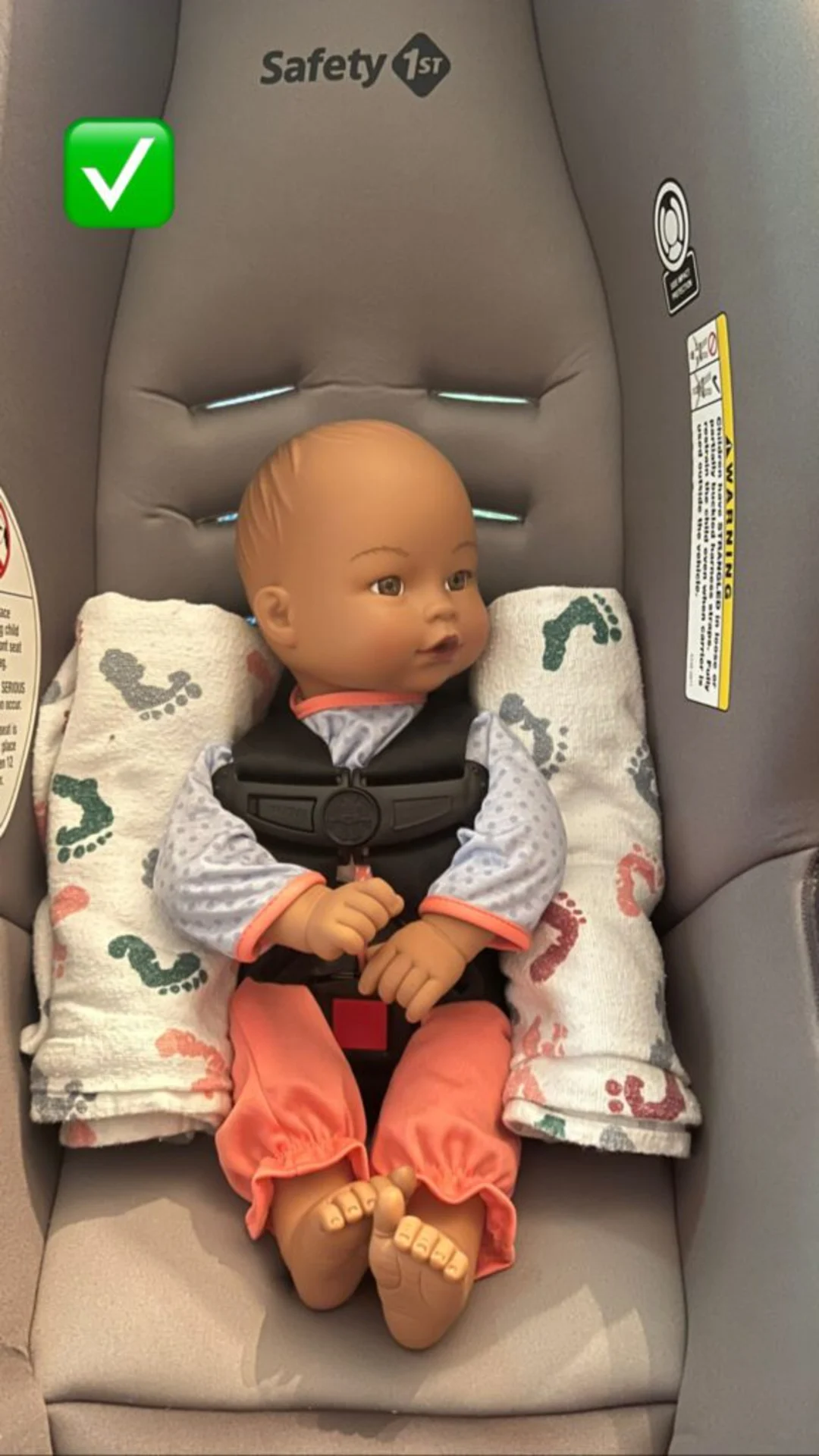 Baby doll correctly buckled in a Safety 1st infant car seat with harness and rolled blanket supports, green checkmark indicat