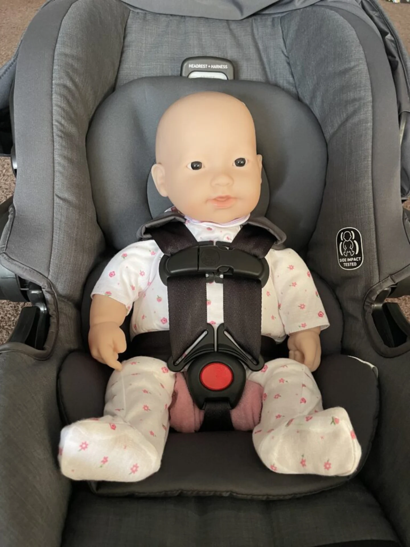 Realistic baby doll wearing floral outfit buckled into a gray side-impact-tested infant car seat with 5-point harness