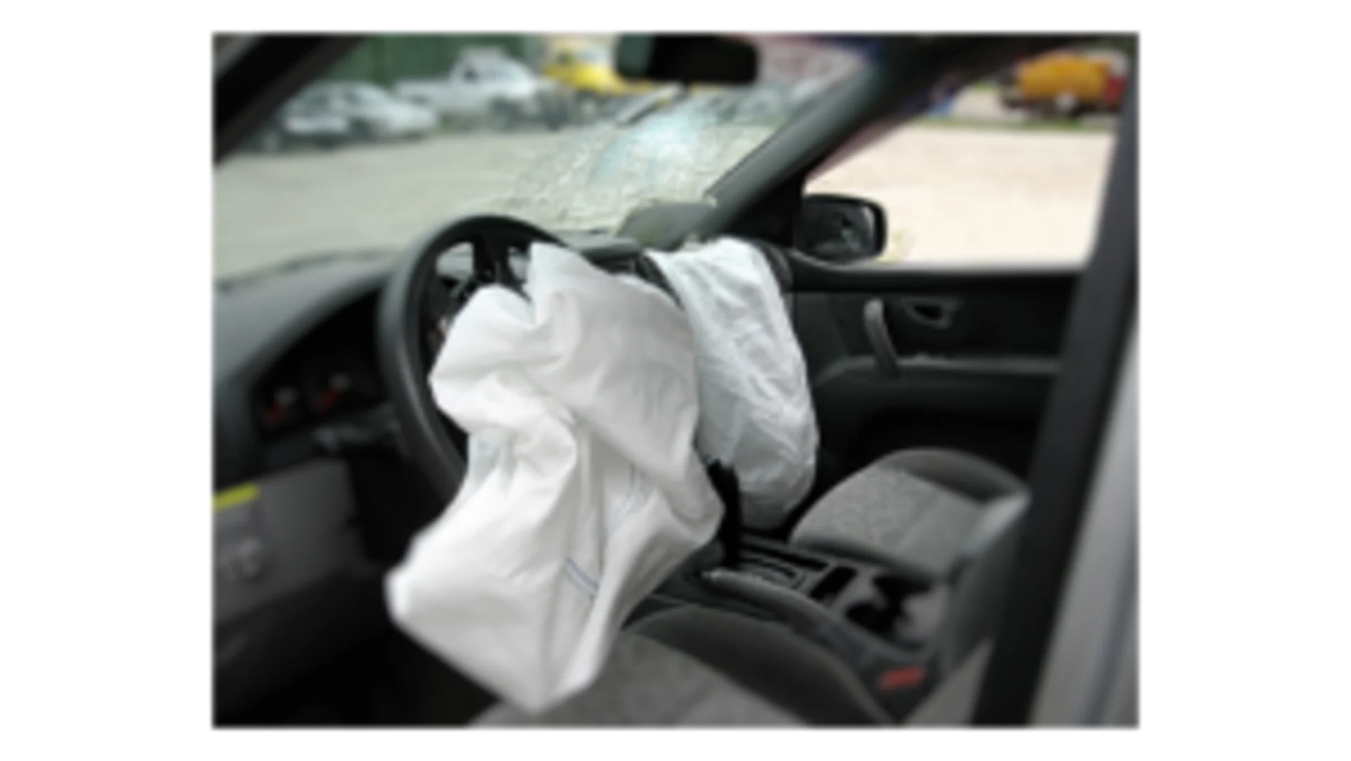 Deployed white driver-side airbag draped over steering wheel after a collision with a cracked windshield visible