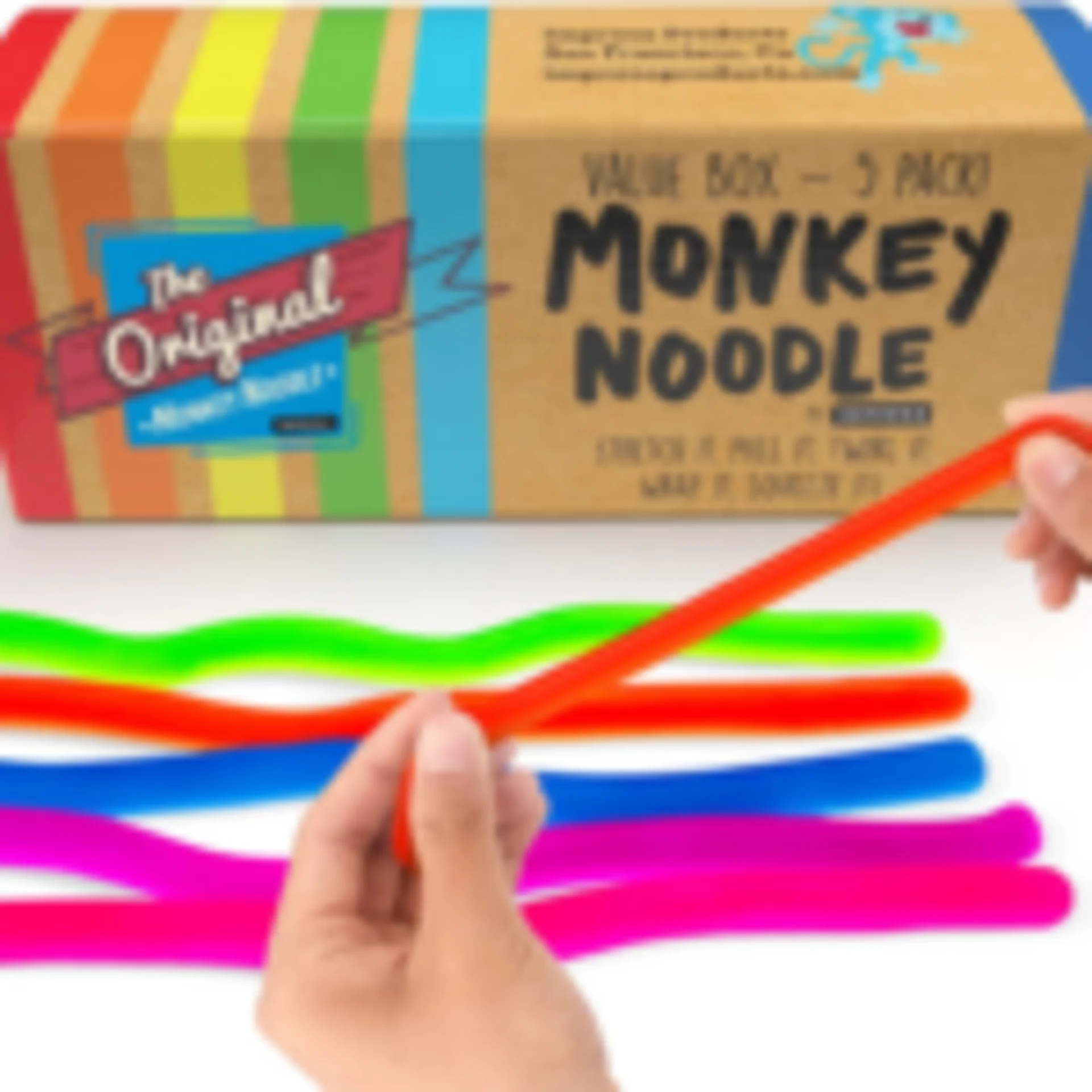 Hands stretching a neon orange Original Monkey Noodle sensory toy with colorful noodles and value box set in background
