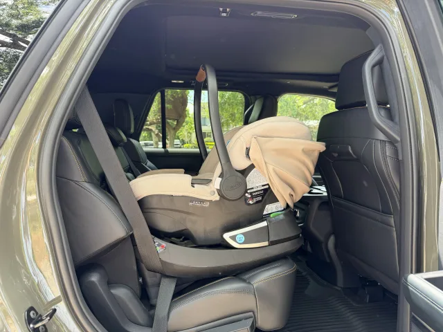 Graco infant car seat with beige canopy installed rear-facing on base in black leather SUV back seat, door open