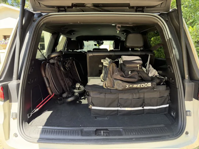 Open SUV cargo area with a folded black stroller, duffel bags, and a black trunk organizer with reflective strip and gold tex