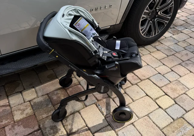 Doona X infant car seat stroller combo in stroller mode with mint green canopy and black 5-point harness on brick pavers besi