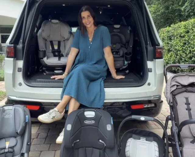 Smiling woman in blue dress sitting in open SUV trunk surrounded by multiple Graco car seats and a stroller for comparison