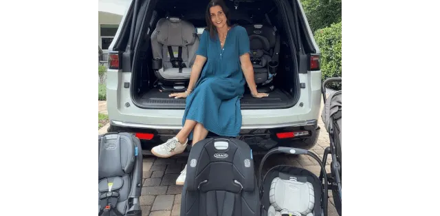 Smiling woman in blue dress sitting in open white SUV trunk surrounded by multiple Graco car seats and a stroller for compari