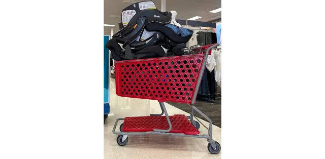 Black infant car seat loaded into a red Target shopping cart inside a retail store during a car seat trade-in recycling event