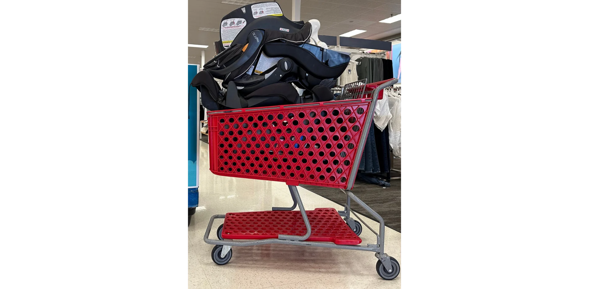 Black infant car seat loaded into a red Target shopping cart inside a retail store during a car seat trade-in recycling event