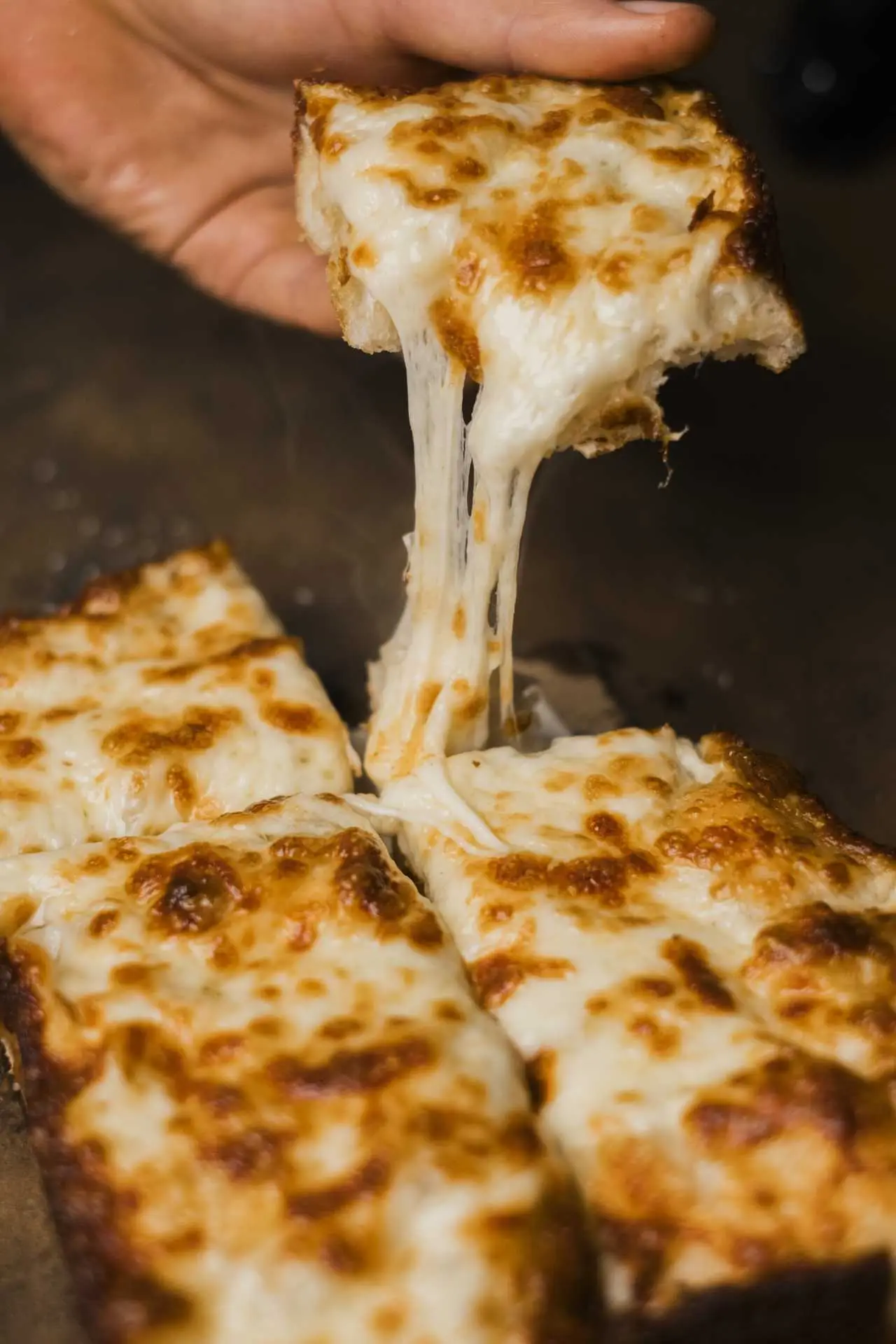 Frissen sült, nyúlós sajtos pizzaszelet, kézzel felemelve, aranybarnára sült ropogós tésztával.