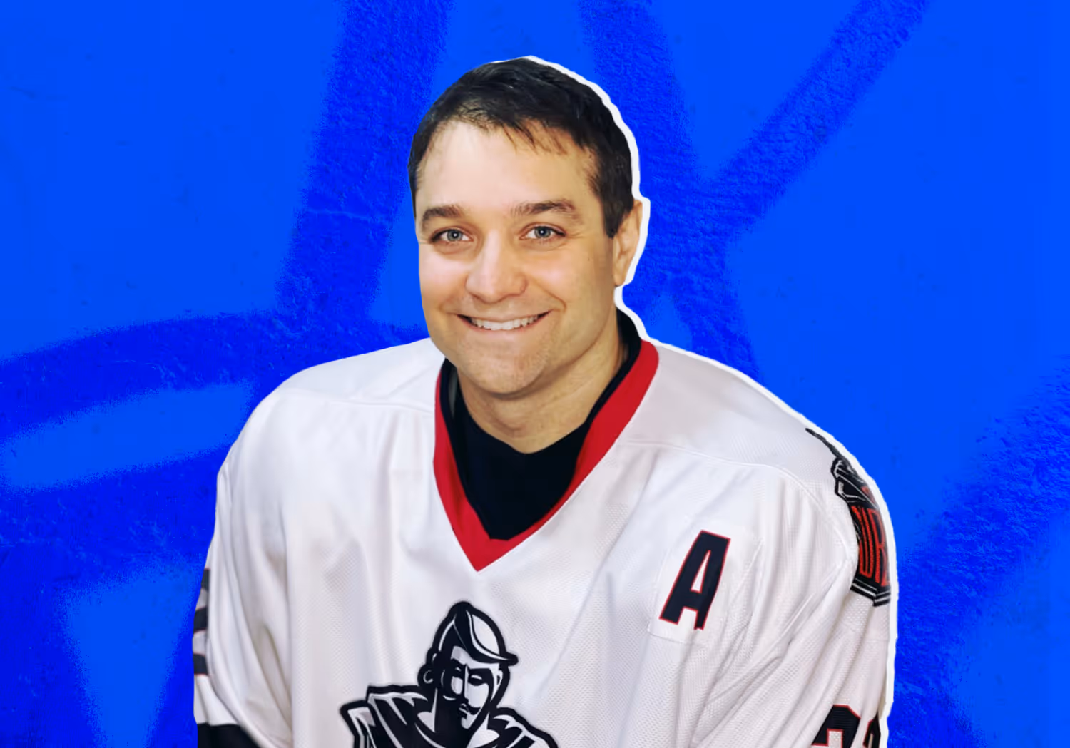 Smiling man wearing a white ice hockey jersey with a red collar and a black logo, standing against a blue background.