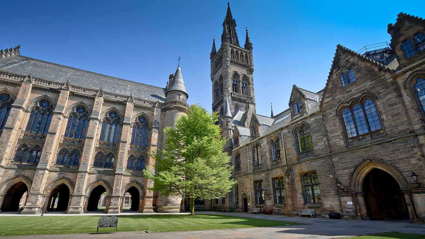 Historic university building with Gothic architecture, arched windows, and a tall clock tower under a clear blue sky.