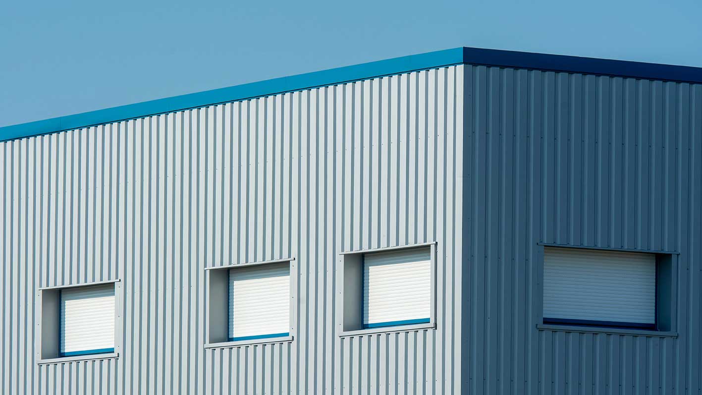Gray industrial building with blue trim and four rectangular windows with closed shutters.