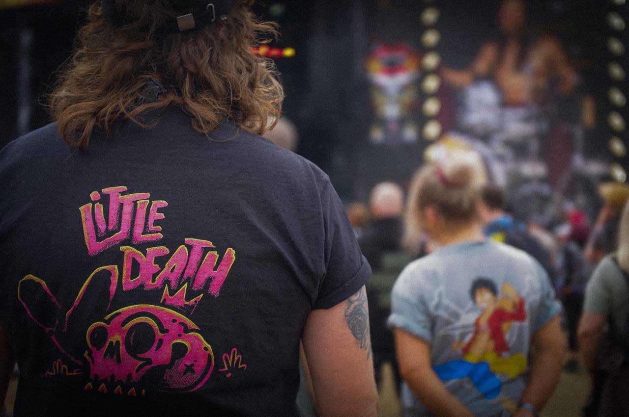 Person with curly hair wearing a black shirt reading 'Little Death' and an illustrated skull on the back.