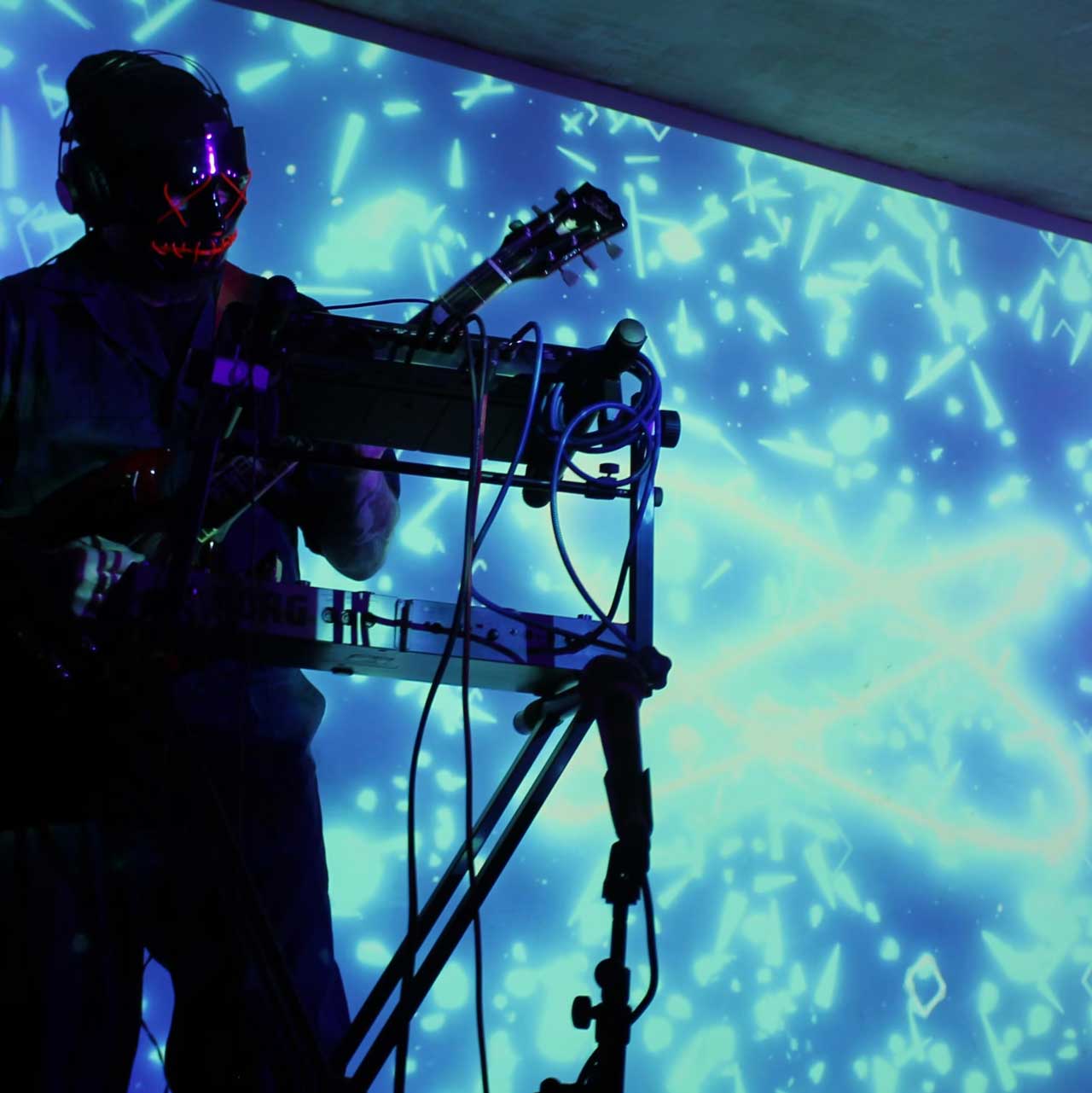 Musician wearing LED-lit mask performing with guitar against a blue abstract light background.