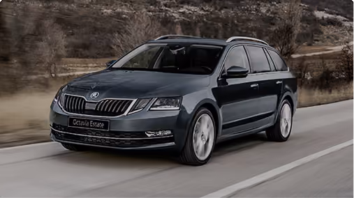 Dark gray Skoda Octavia Estate car driving on a road with blurred background of dry vegetation and hills.
