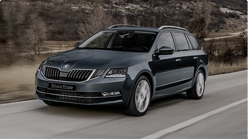 Dark gray Skoda Octavia Estate car driving on a road with blurred background of dry vegetation and hills.