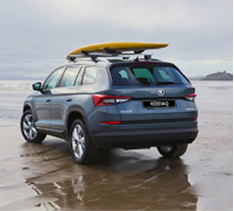 Gray SUV parked on wet sand near the ocean with a yellow surfboard secured on its roof rack under a cloudy sky.