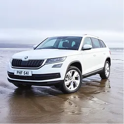 White SUV parked on wet sandy beach under cloudy sky, showing front and side view of the vehicle with visible license plate PHF 541.