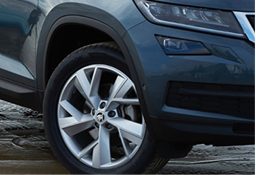 Close-up of a car's front left wheel with a silver alloy rim and tire on a wet surface.