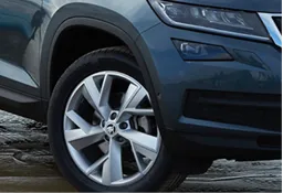 Close-up of a car's front left wheel with a silver alloy rim and tire on a wet surface.