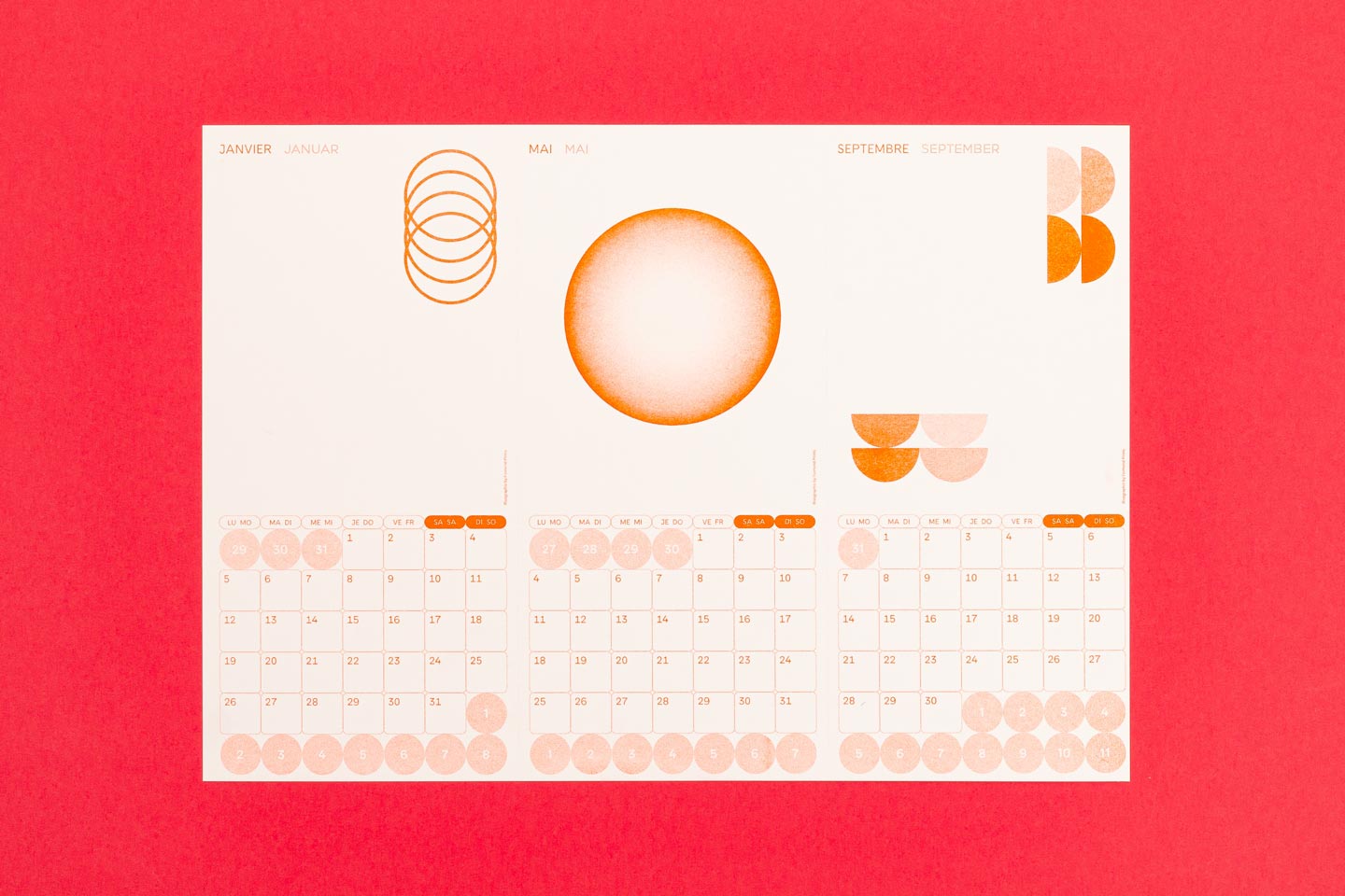 Ein minimalistisches Kalenderdesign mit den Monaten Januar, Mai und September, gestaltet mit künstlerischen orangen Kreisen und geometrischen Formen auf weißem Hintergrund. Der Kalender wurde im Risographieverfahren gedruckt.