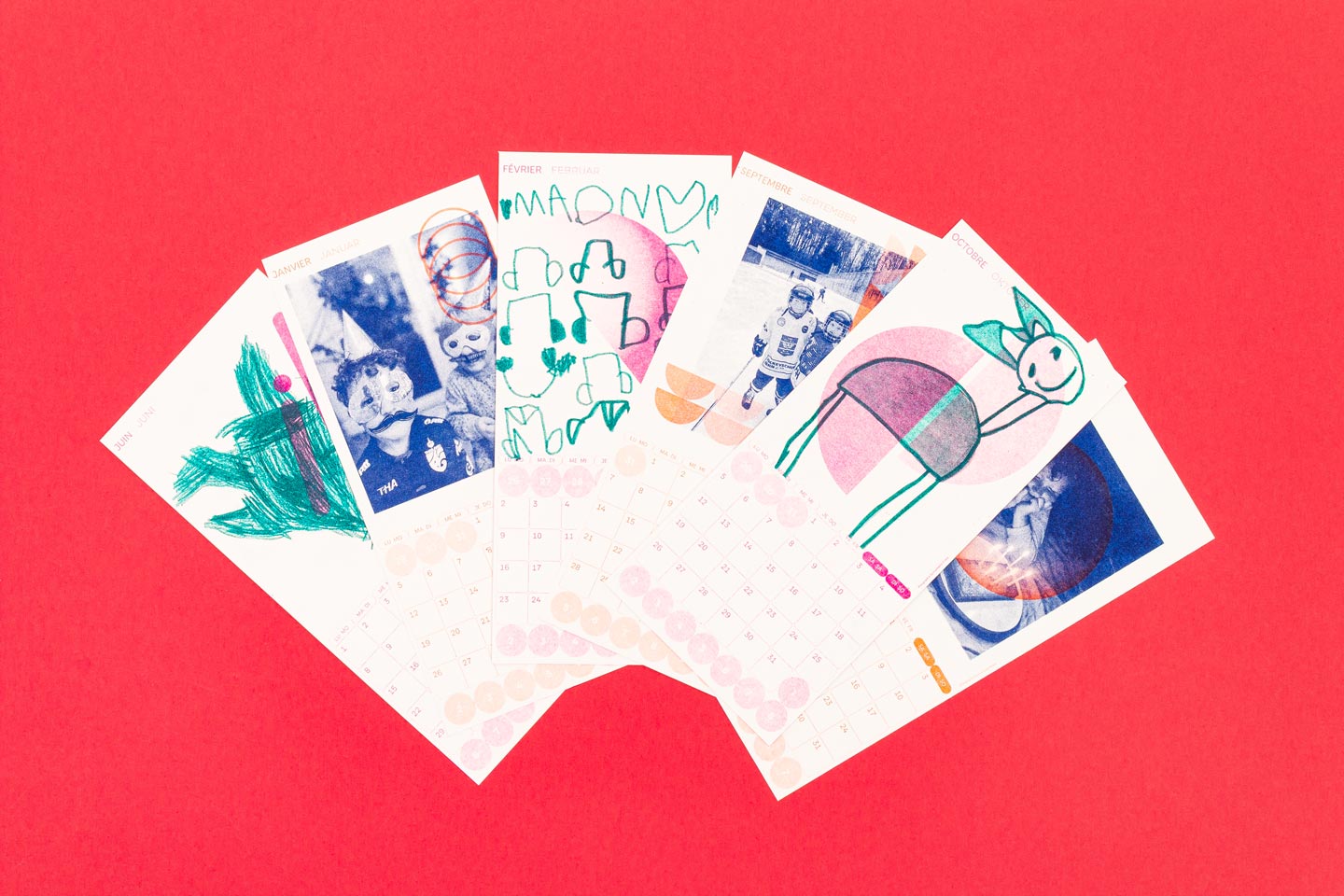 Farbenfrohe Kalenderblätter mit Kinderzeichnungen und Fotos, arrangiert auf einem lebendigen roten Hintergrund. Die Kalender wurden im Risographieverfahren gedruckt.