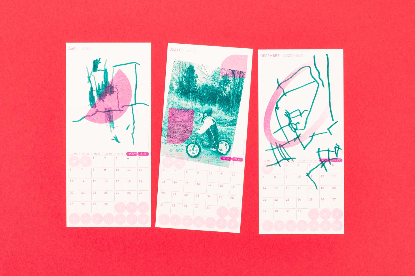 Drei farbenfrohe Kalenderblätter für April, Juli und Dezember mit Kinderzeichnungen und Fotos vor einem lebendigen roten Hintergrund. Die Kalenderseiten wurden im Risographieverfahren gedruckt.