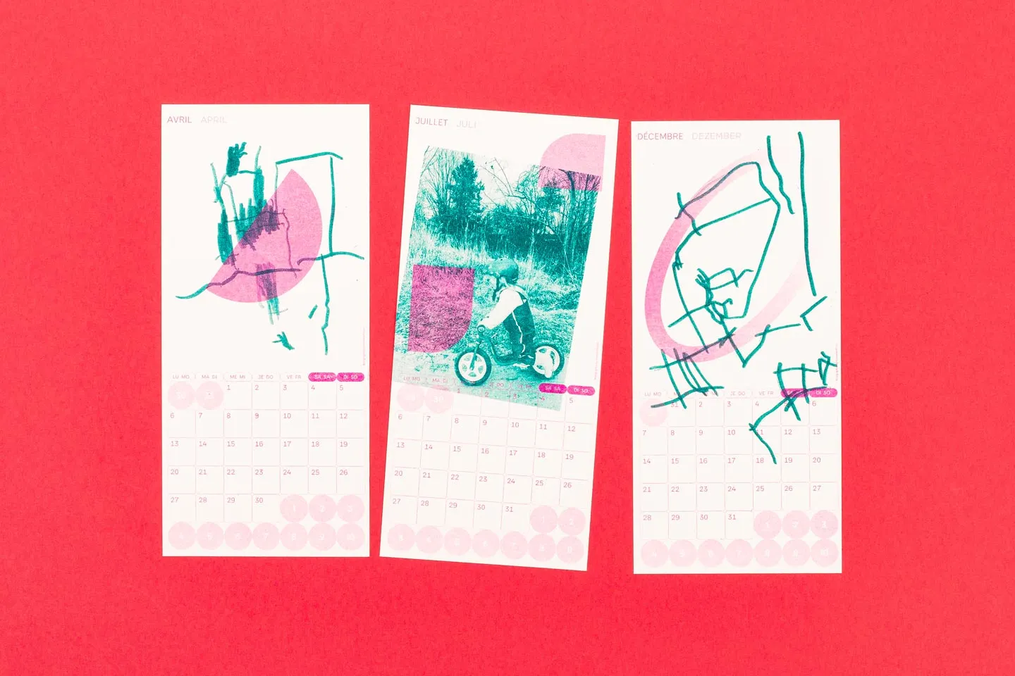 Drei farbenfrohe Kalenderblätter für April, Juli und Dezember mit Kinderzeichnungen und Fotos vor einem lebendigen roten Hintergrund. Die Kalenderseiten wurden im Risographieverfahren gedruckt.