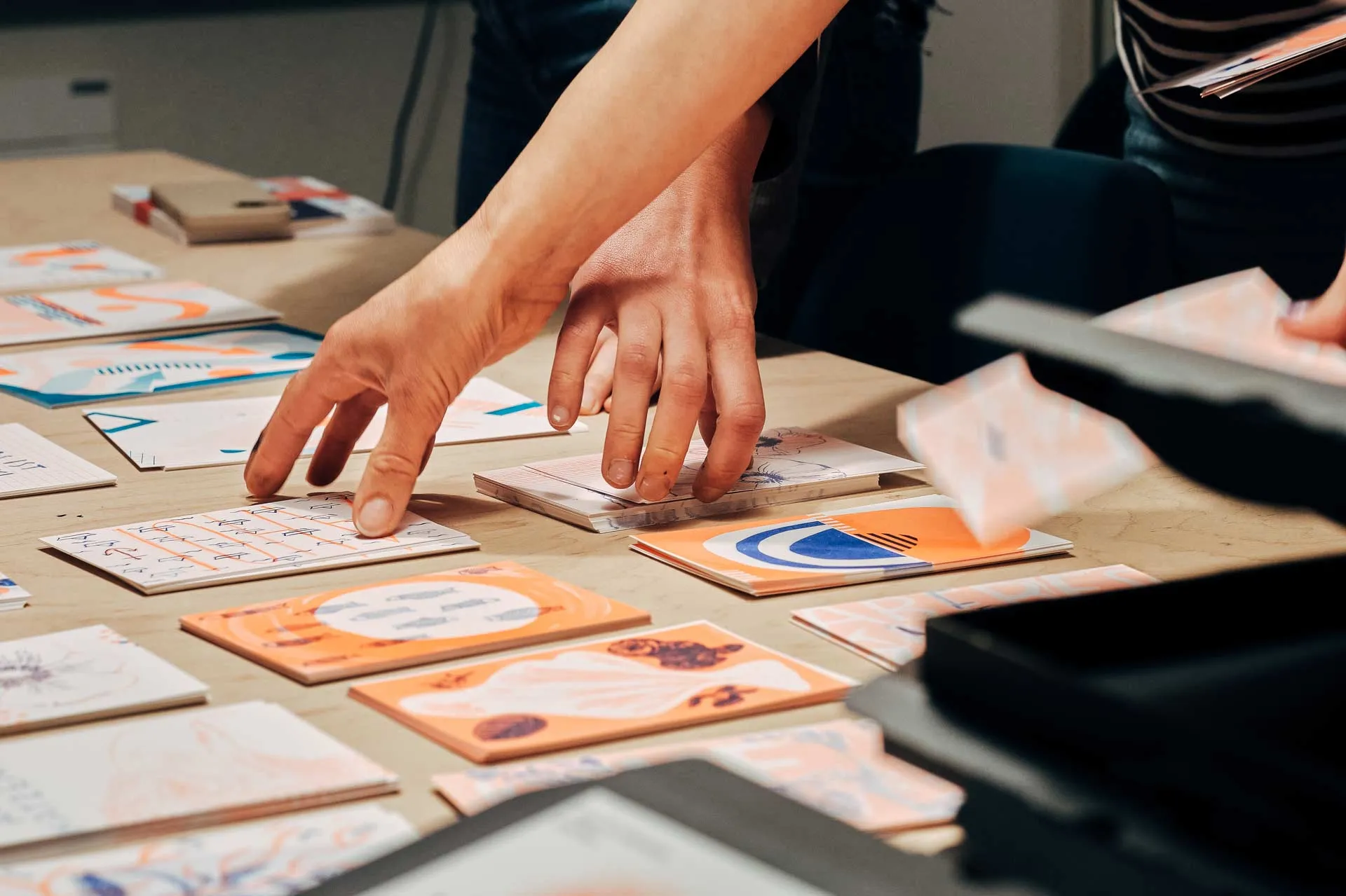 Hände sortieren bunte Risographie-Prints bei Formend – kreative Printproduktion mit charakterstarkem Design.
