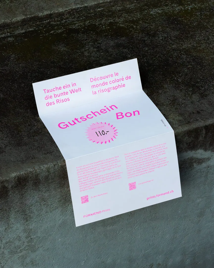 Ein auf einer dunklen Oberfläche liegender, aufgeklappter Gutschein mit pinker Schrift über einen Risographie-Workshop im zweisprachigen Text auf Deutsch und Französisch.