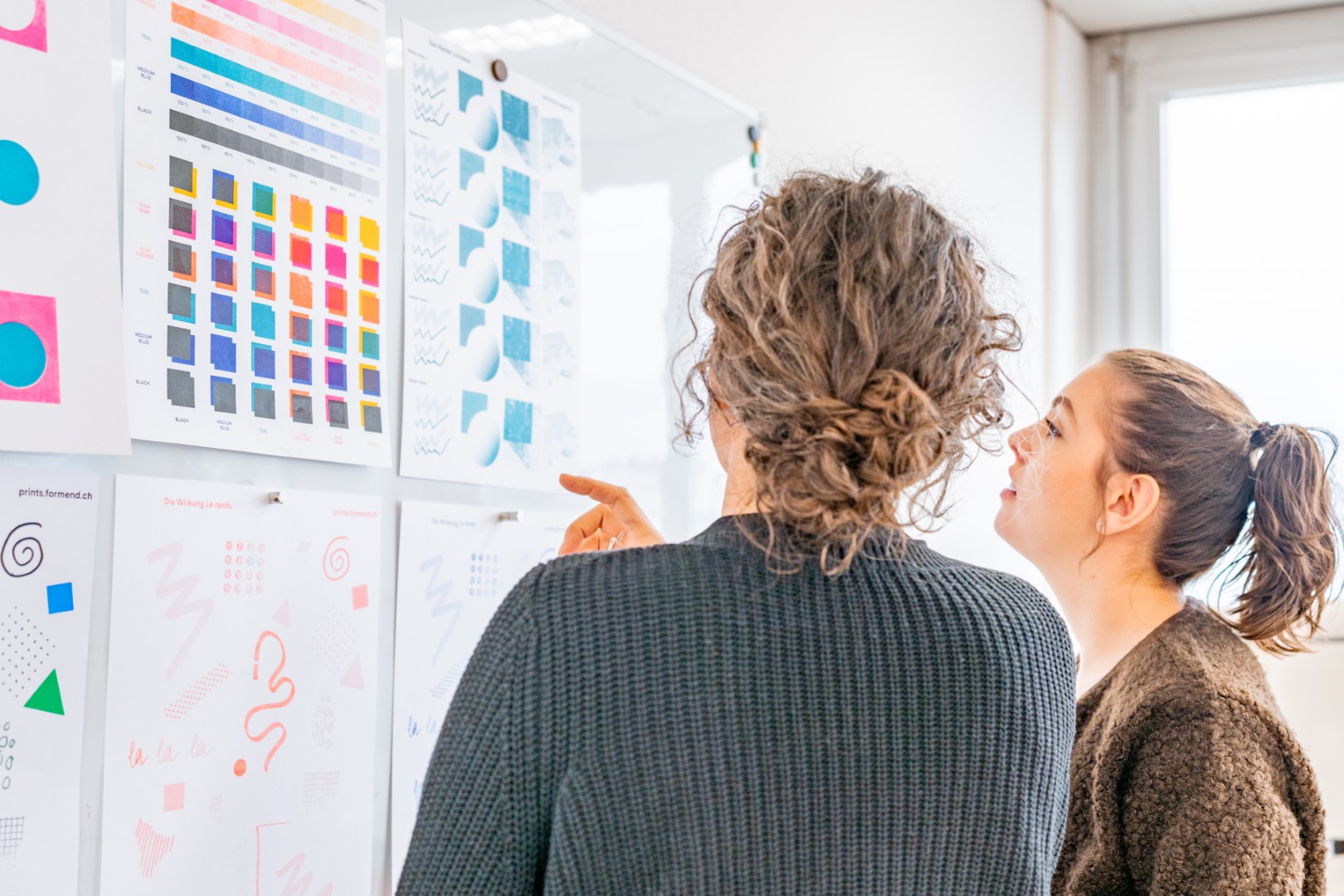 Zwei Frauen betrachten und diskutieren Farb- und Designproben an einer Wand.