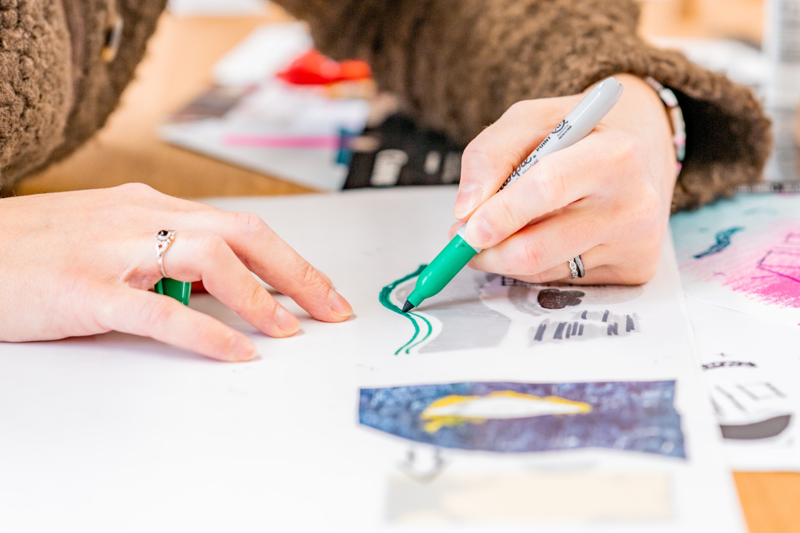 Person zeichnet mit grünem Marker auf einem Blatt Papier mit verschiedenen Skizzen.
