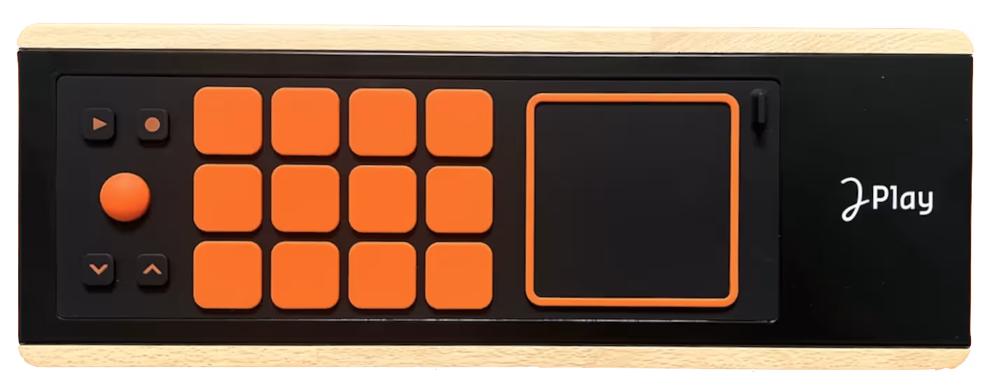 The image shows a Joué Play, a multi-instrument music controller. It features a grid of orange pads, a joystick, and additional control buttons on the left, along with a touch-sensitive pad on the right, all set against a black and wood-like surface. The logo "Joué Play" is displayed on the right side of the device.