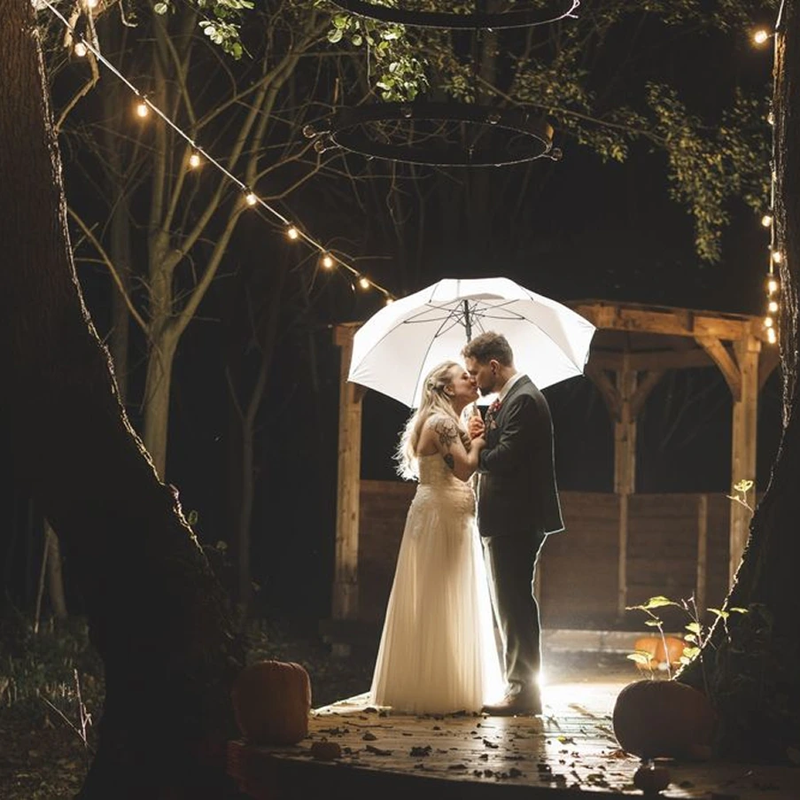 Newlyweds kissing under an umbrella beneath festoon lights at Blackbrook Barns, Lichfield, Staffordshire