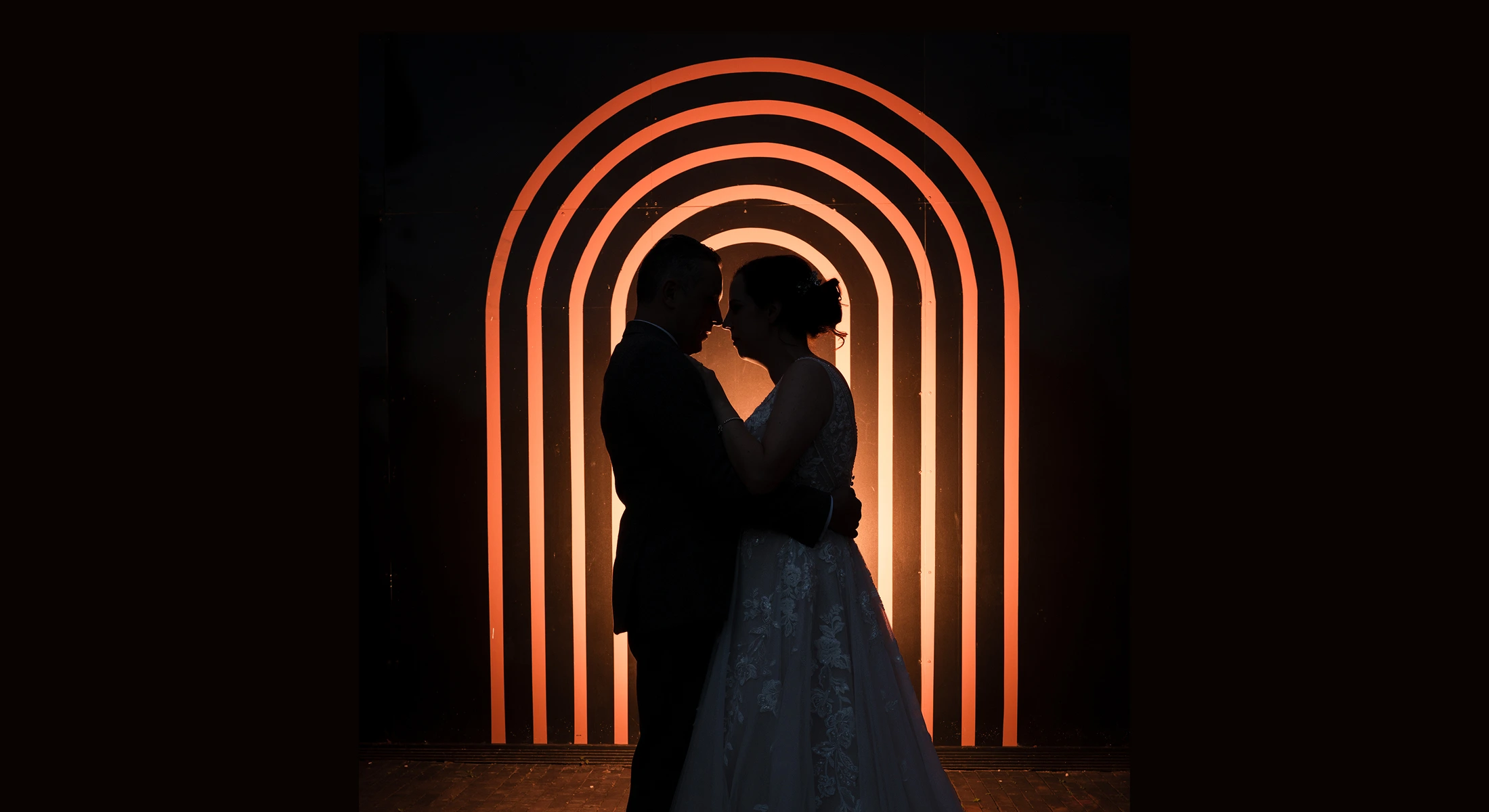 Couple embracing in front of an illuminated arch at a twilight wedding at Blackbrook Barns, Lichfield, Staffordshire