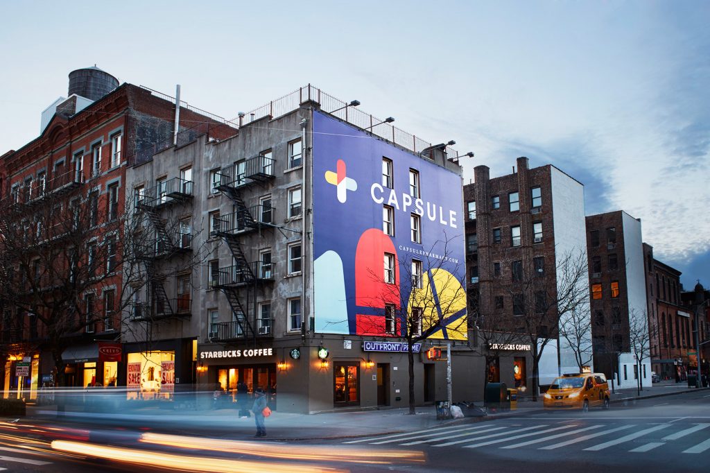 Capsule Pharmacy app poster on side of building with businesses below and cars driving by- M13 Investing