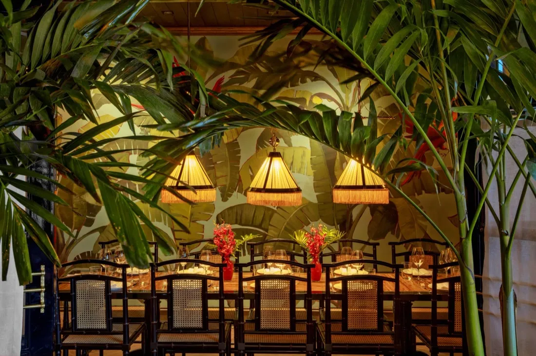 Le Colonial dining room framed by palms, with fringed pendant lamps over a long set table