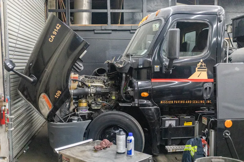 Engine repair with a heavy-duty service truck in a repair bay and the hood raised for maintenance.