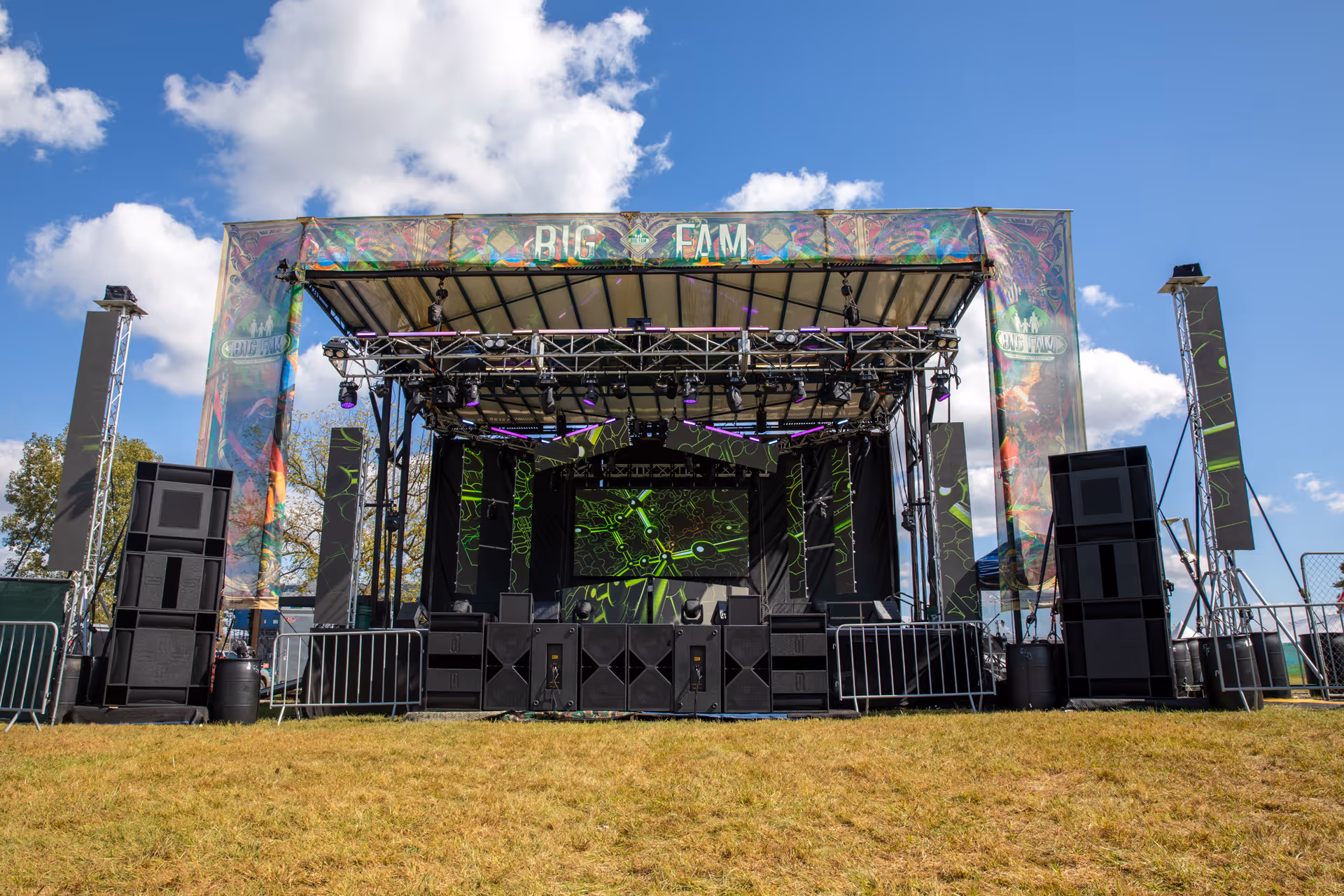 Empty outdoor stage setup with large speakers and lighting under a blue sky with scattered clouds.