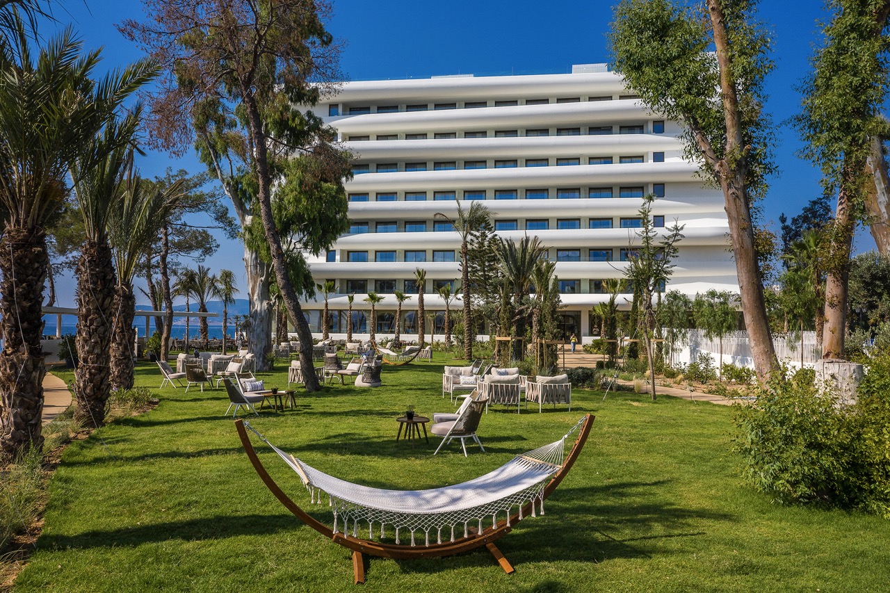 Grüner Garten des Isla Brown Corinthia Resorts mit Hängematte und stilvollen Sitzbereichen vor der weißen Fassade des Hotels.