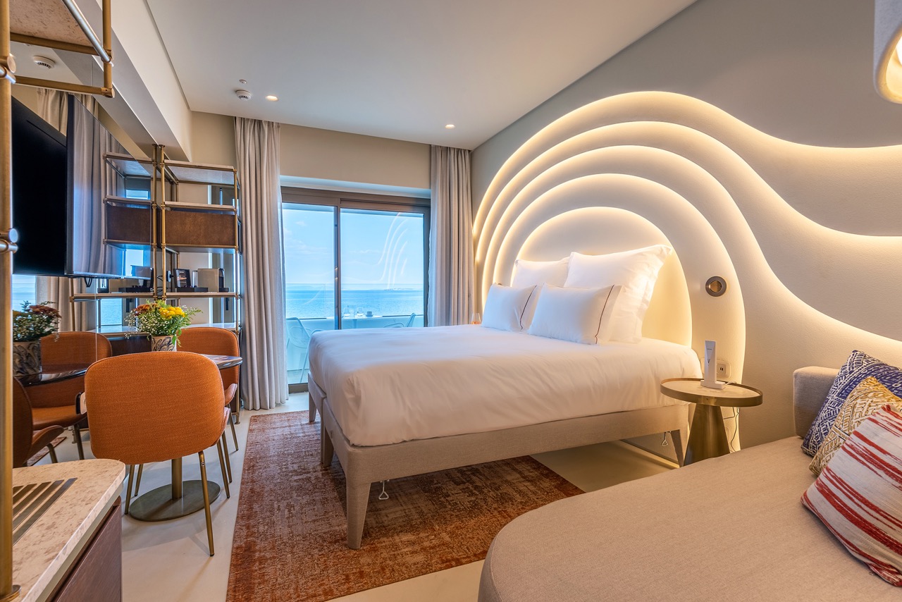 Modernes Deluxe-Zimmer im Isla Brown Corinthia mit Balkon, atemberaubendem Meerblick und stilvollem, wellenförmigem Design.