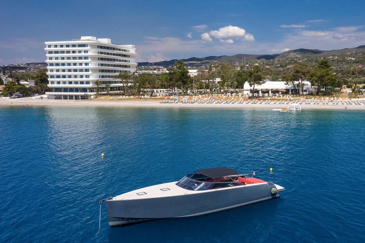 Isla Brown Corinthia Resort: Moderne Architektur mit direkter Strandlage, kristallklarem Wasser und einem eleganten Boot im Vordergrund.
