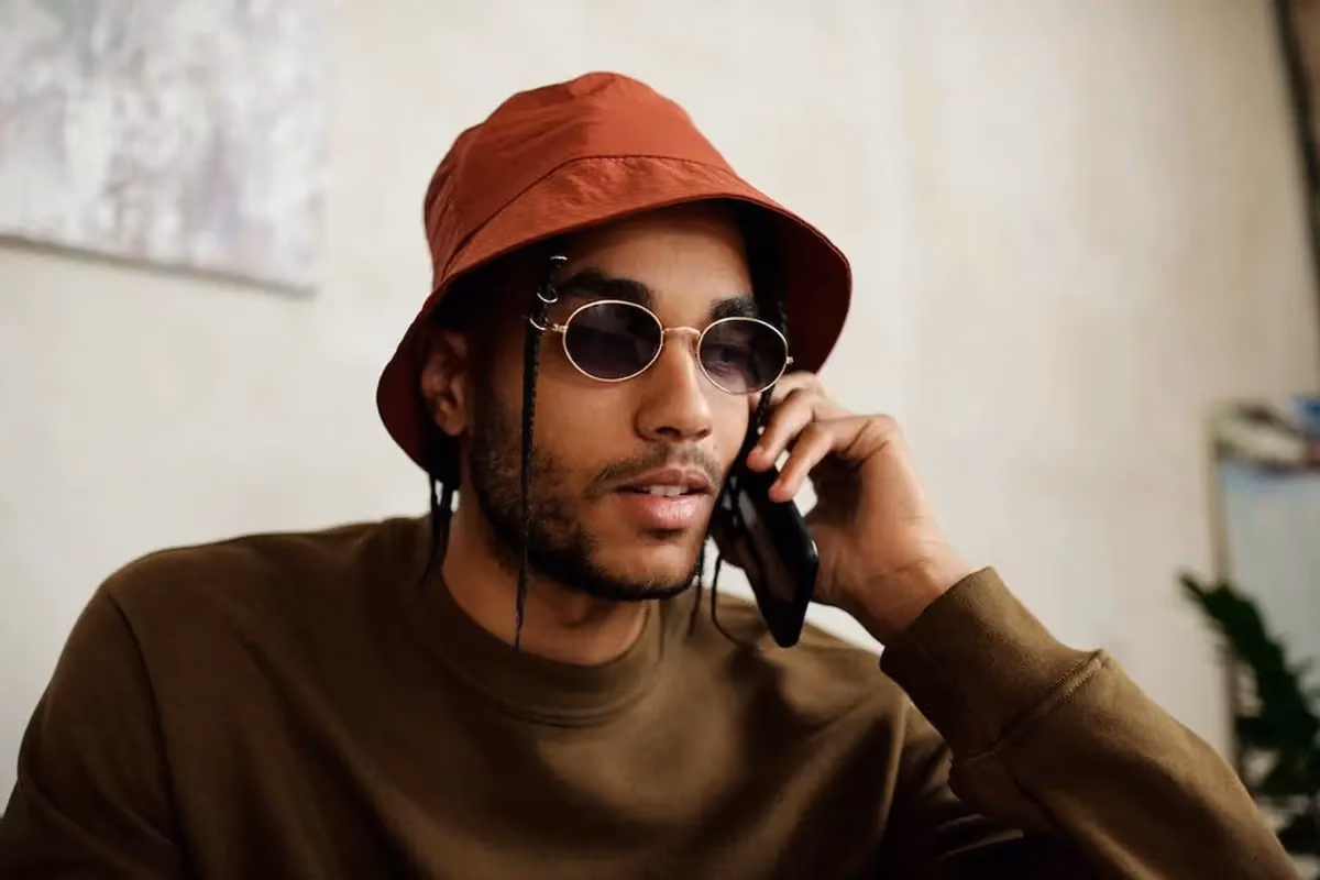 a person wearing a hat and sunglasses talking on a phone
