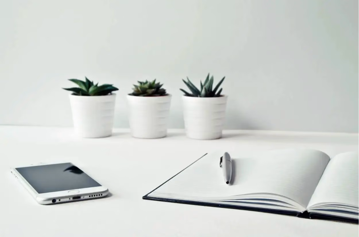 a pen on a notebook next to a phone and potted plants