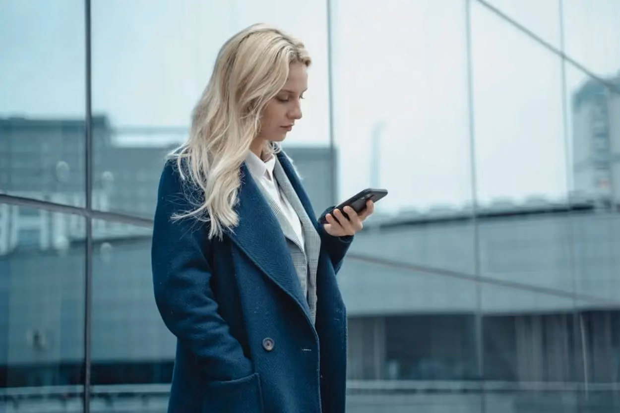 a woman standing in a coat looking at a phone