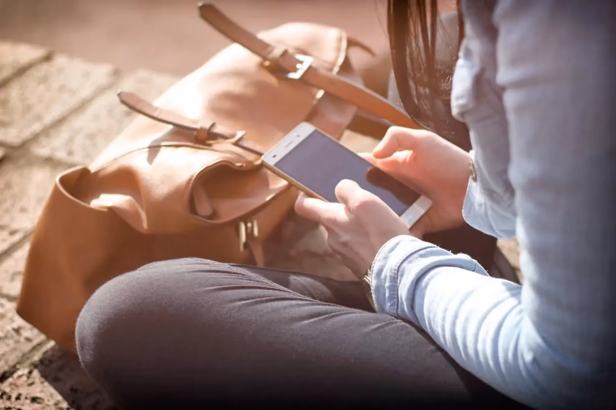 a person sitting on a rock looking at a cell phone