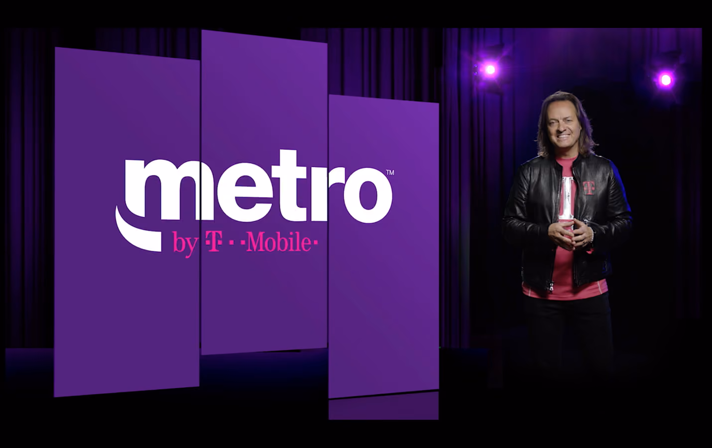 A man stands before a purple screen displaying the logo and text for Metro by T-Mobile.