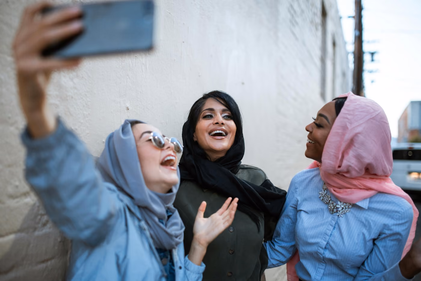 Three women in headscarves smiling together while taking a selfie, capturing a moment of friendship and joy.