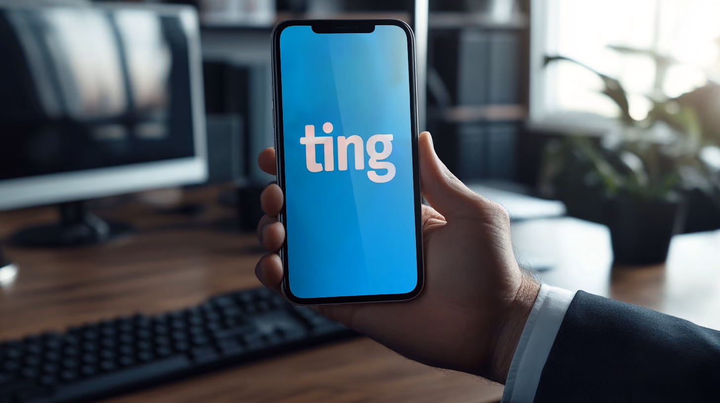 Hand holding an smartphone with Ting Mobile logo on the screen in their office